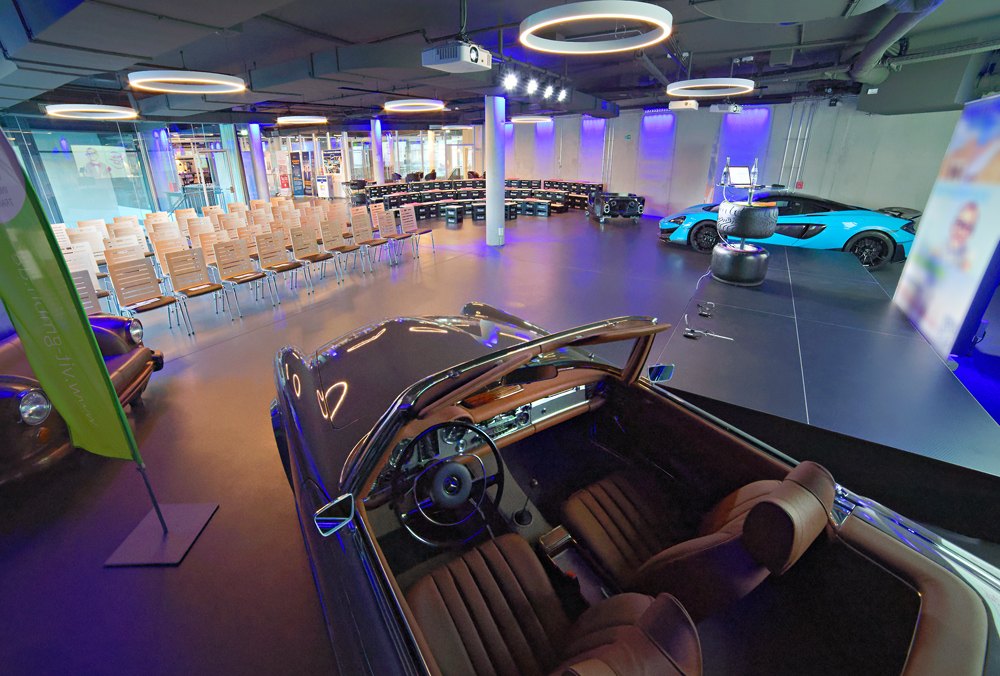 Eventfläche im V8 Hotel mit Stuhlreihen, Bühne und Fahrzeugen